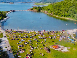 St. Hans fairing hos Geitvågen Camping! Stort bål på en gresslette med folk som myldrer nært vannet.